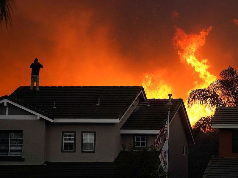 Herman Termeer, 54, stands on the roof of his home as the Blue Ridge Fire burns along the hillside Tuesday, Oct. 27, 2020, in Chino Hills, Calif. Image Credit: AP